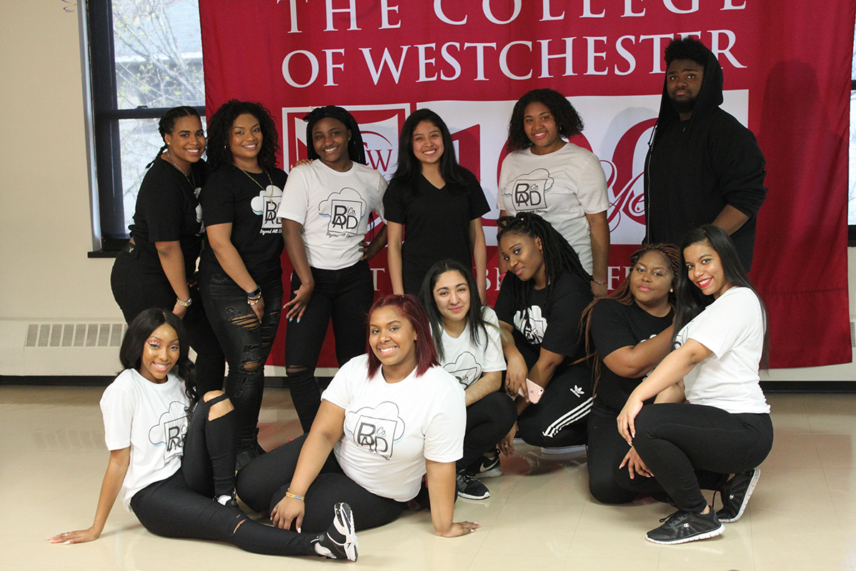 Members of the College of Westchester Just Dance Crew posing together in matching black and white crew t-shirts in front of a College of Westchester banner