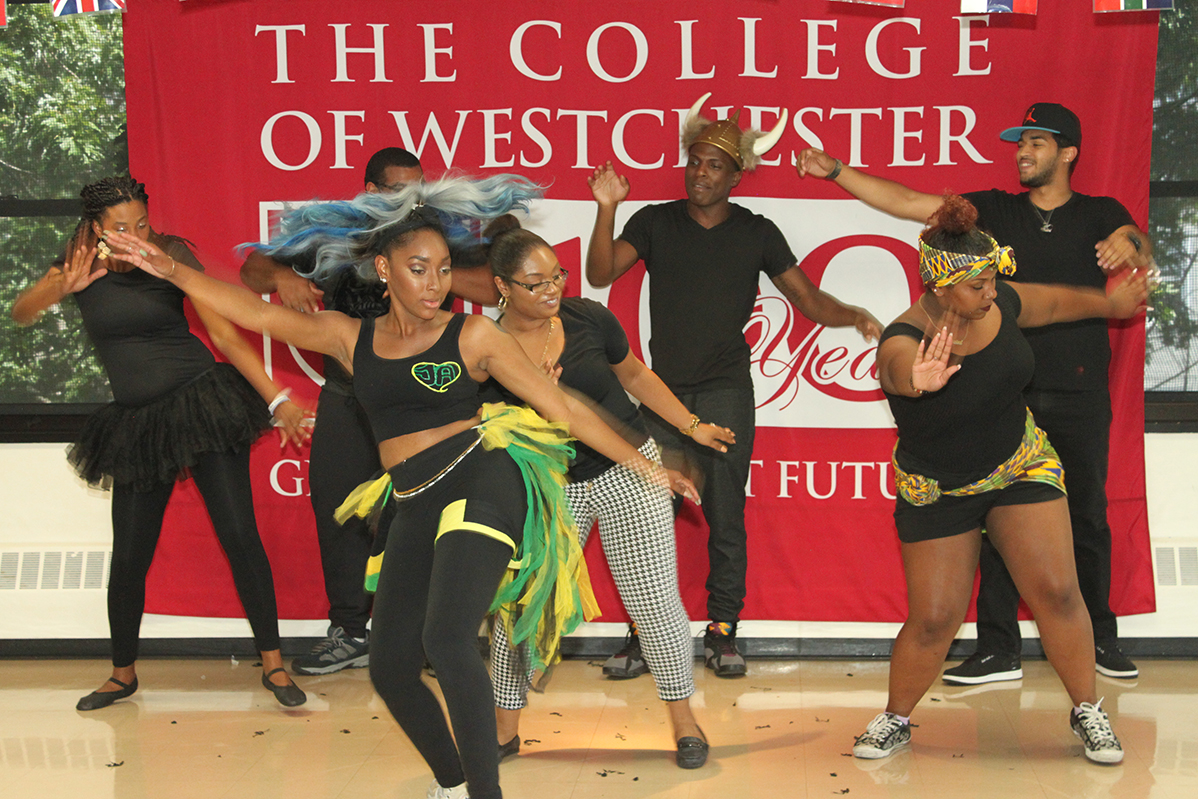 College of Westchester Just Dance Crew members mid-performance in front of a College of Westchester banner, wearing colorful coordinated costumes